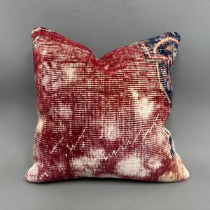 May include: Red and blue patterned throw pillow with a faded, distressed look. The pillow is made of a soft, woven fabric.
