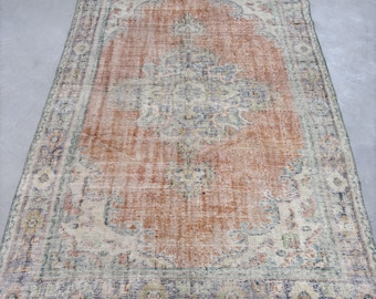 May include: A vintage rug with a faded orange background and a detailed floral pattern in shades of blue, green, and beige. The rug has a distressed look and a worn border.