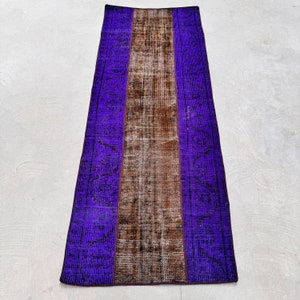 May include: A rectangular, vintage rug with a central brown stripe flanked by vibrant purple borders. The rug features a distressed, faded appearance, with visible wear and tear adding to its character. The design includes subtle patterns within the purple sections.