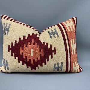 May include: A decorative throw pillow with a geometric pattern in shades of red, orange, and cream. The pillow has a woven texture and a fringe border.