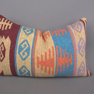 May include: A decorative pillow with a colorful geometric pattern in shades of red, orange, blue, and purple. The pillow is made of a woven fabric with a textured surface.