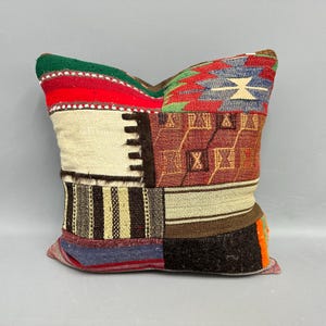 May include: A patchwork pillow with a variety of colors and patterns. The pillow features sections of red, green, white, brown, and blue fabrics. The design includes geometric shapes and textured weaves, creating a rustic, handcrafted aesthetic.