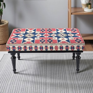 May include: A rectangular ottoman with a patterned top featuring red, blue, and cream geometric designs. The ottoman has a black frame and four black, turned legs. The design is reminiscent of a traditional rug.