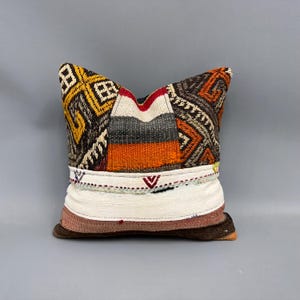May include: A colorful patchwork pillow with a white border and geometric patterns in shades of brown, orange, red, and yellow.