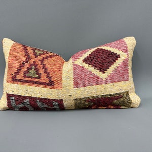 May include: A rectangular pillow with a geometric pattern in shades of red, pink, and cream. The pillow is made of woven fabric and has a fringed edge.