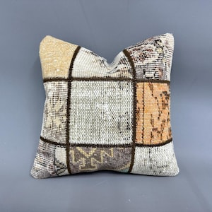 May include: A square patchwork pillow with a beige, brown, and orange color scheme. The pillow is made of woven fabric and has a variety of patterns.