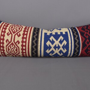 May include: A long, rectangular pillow with a colorful geometric pattern. The pillow is made of woven fabric and features a variety of colors, including red, blue, black, and white.