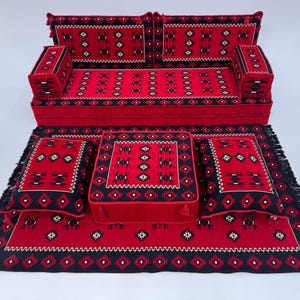 May include: A red and black patterned sofa set with matching cushions and a rug. The set features a geometric design with white accents. The rug has a fringed edge, and the cushions are square and rectangular.