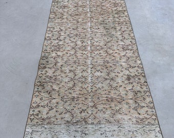 May include: A vintage runner rug with a floral pattern in shades of beige, brown, and white. The rug has a fringed edge and a subtle distressed look.