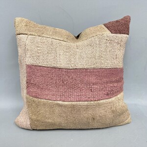 May include: Square decorative pillow with a patchwork design. The pillow features horizontal stripes in beige and dusty rose colors. The pillow is made of a textured fabric, likely woven.