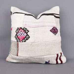 May include: White patchwork pillow with geometric designs in pink, blue, and black. The pillow features a variety of fabric patches, with black and burgundy stripes on the bottom. A decorative accent for a sofa or bed.