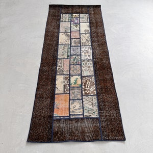 Puede incluir: Una alfombra larga y rectangular con un fondo marrón y un panel central de cuadrados de patchwork coloridos. Los cuadrados de patchwork están dispuestos en una columna vertical y presentan una variedad de patrones y colores, incluyendo diseños florales, geométricos y abstractos.