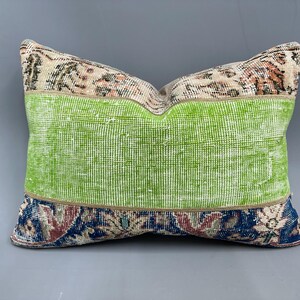 May include: A green, blue, and beige patterned throw pillow with a green center panel. The pillow is made from a woven fabric with a distressed look.