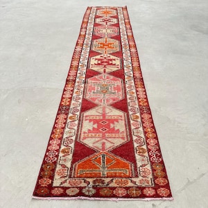 Peut inclure: Un tapis de couloir rouge, orange et blanc à motifs géométriques. Le tapis a une bordure frangée.