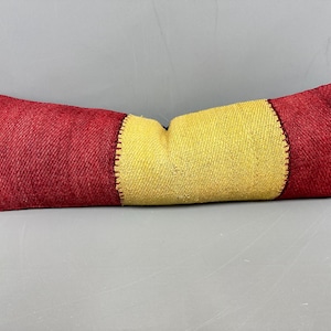 May include: A rectangular pillow with a color block design. The pillow features a central yellow section flanked by two red sections. The sections are sewn together with a contrasting stitch. The pillow is likely made of woven fabric.