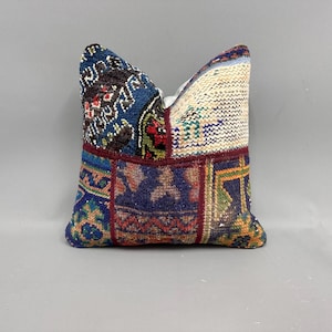 May include: A patchwork pillow cover with a variety of colors and patterns, including blue, red, green, and white. The pillow cover is made of a woven fabric and has a square shape.