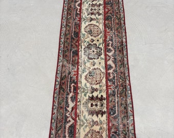 May include: A vintage runner rug with a cream background and red, blue, and green floral patterns. The rug has a fringed edge.