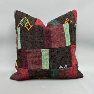 May include: A colorful, striped throw pillow with a geometric pattern in shades of brown, red, green, and yellow. The pillow is made of woven fabric and has a rectangular shape.