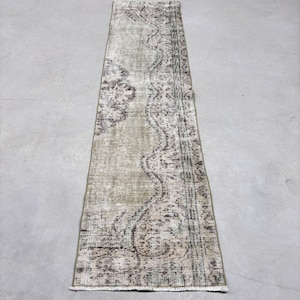 May include: A vintage runner rug with a faded green background and a brown and white floral pattern. The rug has a fringed edge.