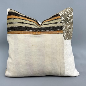 May include: A patchwork pillow with a white background and brown, orange, and beige stripes. The pillow has a floral pattern on one side.