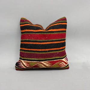May include: A striped pillow cover with a woven design in shades of red, orange, green, and black. The pillow cover has a decorative border with a wave pattern.