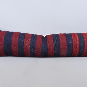 May include: A long, rectangular pillow with a striped pattern in navy blue and burgundy. The pillow is made of a textured fabric and has a slightly distressed appearance. The pillow measures approximately 40 inches in length.