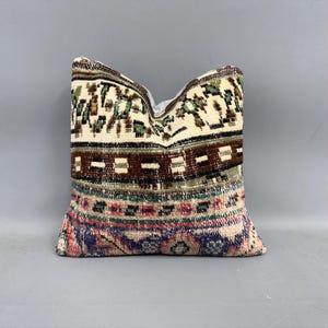 May include: A decorative pillow with a colorful geometric pattern in shades of brown, green, blue, pink, and white. The pillow is made of woven fabric and has a fringed edge.