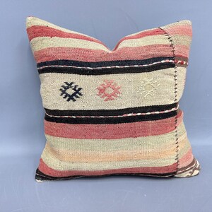 May include: Square decorative pillow with a woven design. The pillow features horizontal stripes in shades of pink, black, and cream. It has embroidered floral and geometric patterns. The pillow is approximately 18 inches square.