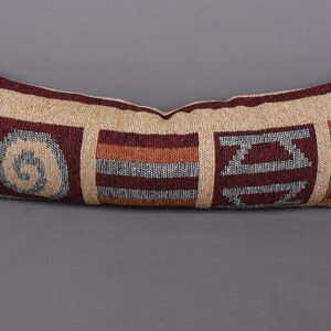 Peut inclure: Un long coussin rectangulaire avec un fond beige et un motif géométrique dans les tons de brun, rouge et gris. Le motif présente une spirale, des rayures et des formes abstraites.