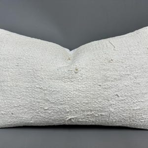 May include: A white, textured pillow with a slightly distressed look. The pillow is made of a soft, woven fabric and has a rectangular shape.