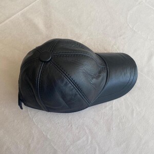 May include: A black leather baseball cap with a stitched design. The cap has a button on the top.
