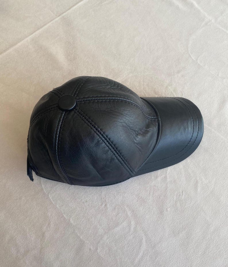 May include: A black leather baseball cap with a stitched design. The cap has a button on the top.