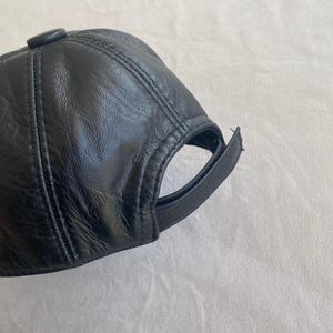May include: A black leather baseball cap with a stitched design. The cap has a curved brim and a button on top.