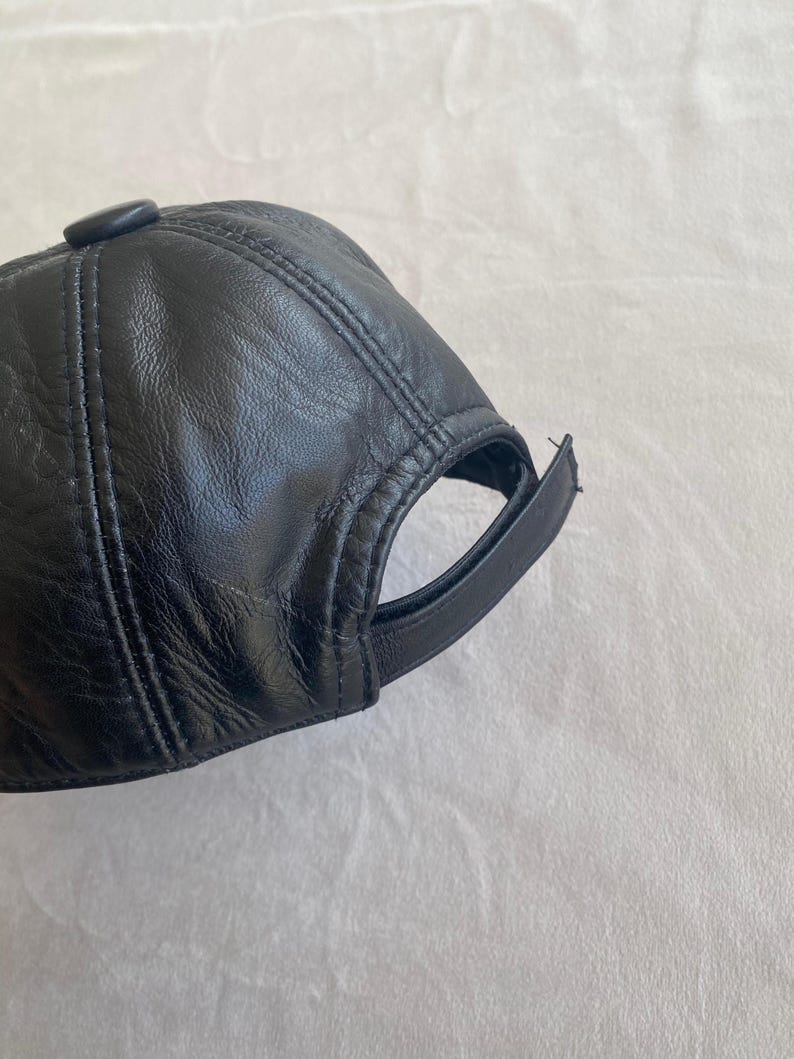 May include: A black leather baseball cap with a stitched design. The cap has a curved brim and a button on top.