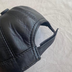 May include: A black leather baseball cap with a button on the top and an adjustable strap in the back.