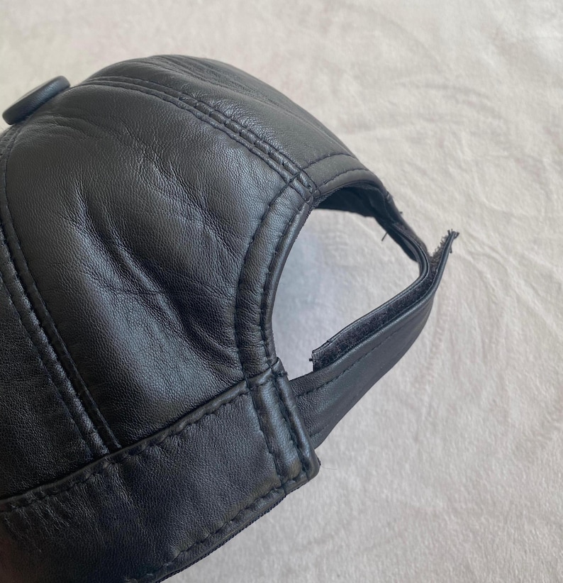 May include: A black leather baseball cap with a button on the top and an adjustable strap in the back.