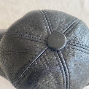 May include: Black leather baseball cap with a stitched design and a button on the top.
