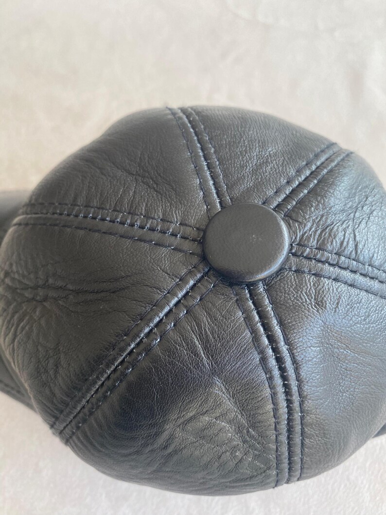 May include: Black leather baseball cap with a stitched design and a button on the top.
