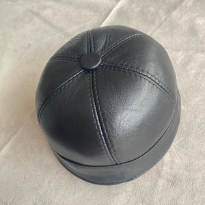 May include: A black leather newsboy cap with a stitched design and a button on top.