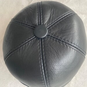 May include: A black leather cap with a stitched design. The cap has a round shape and a smooth surface.