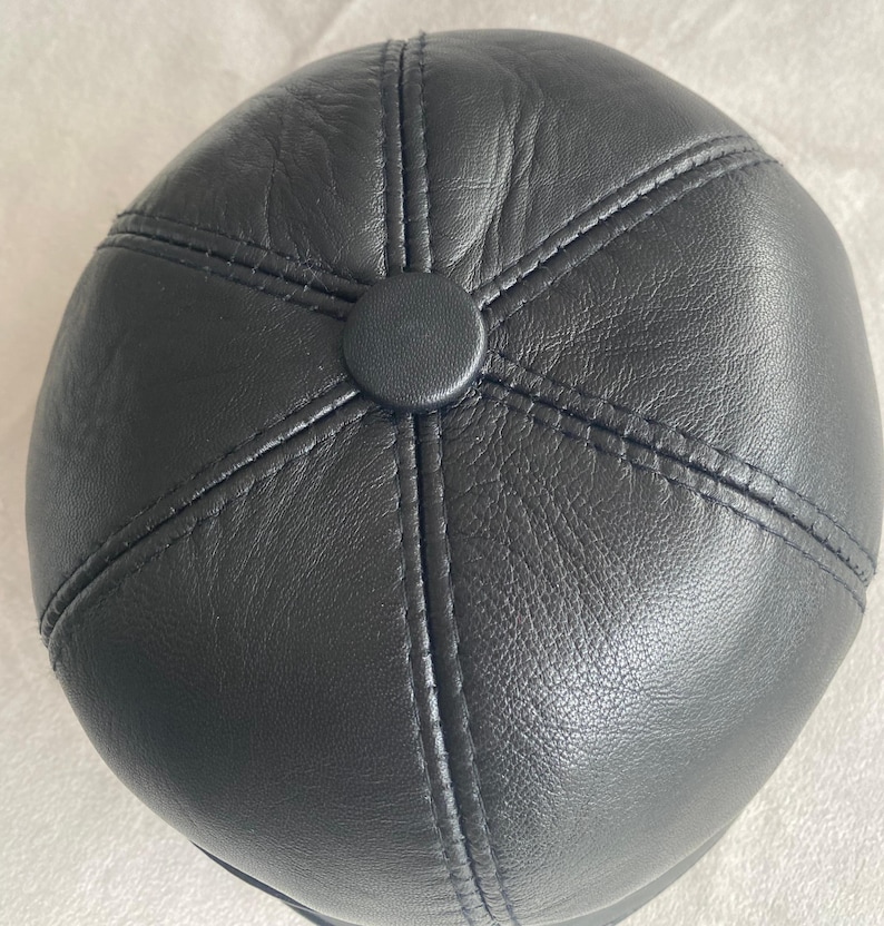 May include: A black leather cap with a stitched design. The cap has a round shape and a smooth surface.