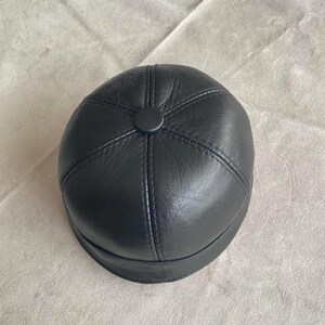 May include: A black leather cap with a round crown and a stitched design. The cap has a button on the top.