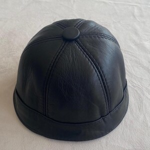 May include: A black leather dome-shaped hat with a button on top.