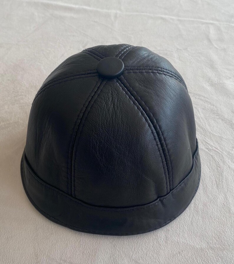 May include: A black leather dome-shaped hat with a button on top.