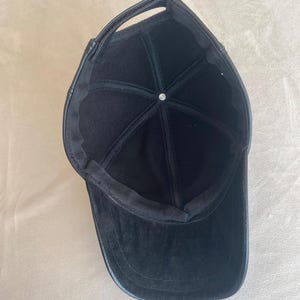 May include: Black leather baseball cap with a curved brim. The cap has a black fabric lining.