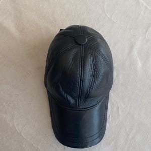 May include: A black leather baseball cap with a stitched design and a button on top.
