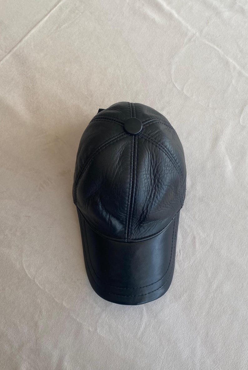 May include: A black leather baseball cap with a stitched design and a button on top.