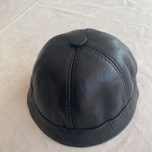 May include: A black leather baseball cap with a stitched design and a small black button on top.