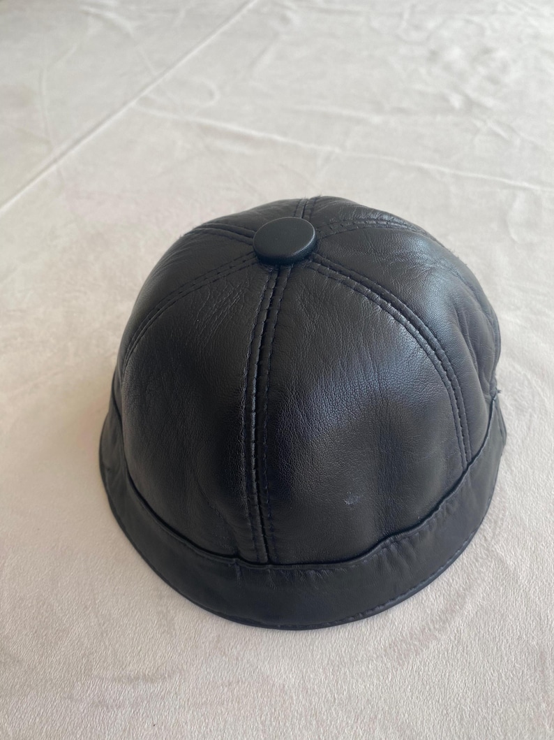 May include: A black leather baseball cap with a stitched design and a small black button on top.