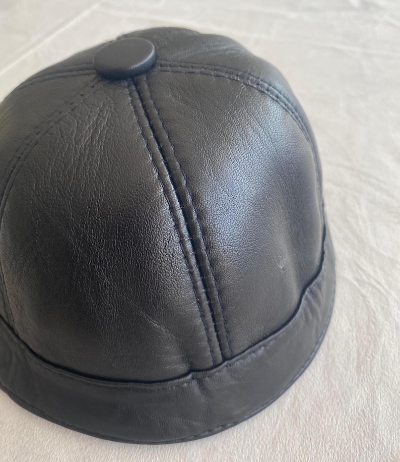 May include: A black leather baseball cap with a button on top.